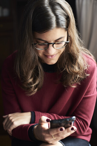 Lächelnde junge Frau schaut auf ihr Handy, lizenzfreies Stockfoto