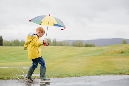 Rothaariger kleiner Junge mit Regenschirm spielt im Regen - NMS00298