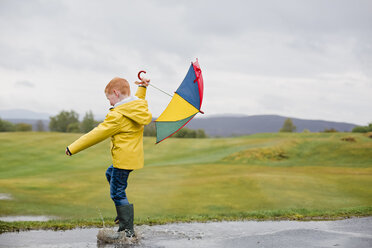 Rothaariger kleiner Junge mit Regenschirm spielt im Regen - NMS00299