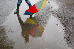 Kleiner Junge mit Regenschirm und Gummistiefeln steht in einer Pfütze, Teilansicht - NMS00300