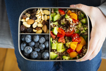 Girl holding a lunchbox with quinoa salad, blue berry and trail mix - LVF07830