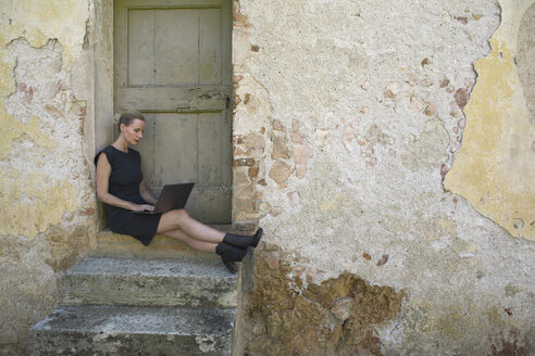 Italien, Toskana, Monteriggioni, Frau sitzt am Hauseingang und benutzt Laptop - PSTF00298