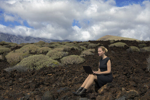 Spanien, Teneriffa, Malpais de Guimar, Frau sitzt in Vulkanlandschaft mit Kakteen und benutzt Laptop - PSTF00311