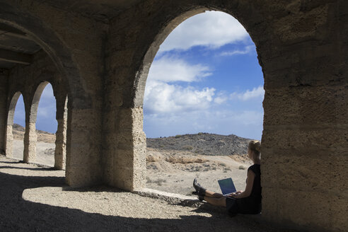 Spanien, Teneriffa, Abades, Sanatorio de Abona, Frau sitzt in einem Geisterstadtgebäude und benutzt einen Laptop - PSTF00318