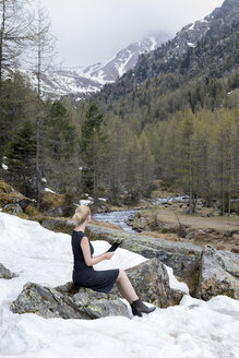 Italien, Südtirol, Ultental, Frau sitzt in einem schneebedeckten Bergtal und benutzt ein Tablet - PSTF00320