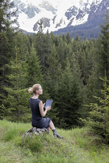 Italien, Südtirol, Welschnofen, Frau sitzt in Berglandschaft und benutzt Tablet - PSTF00321