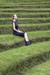 Italy, Alto Adige, Lana, woman sitting on grass-covered steps of natural open air theater - PSTF00325