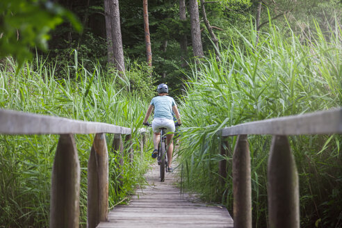 Frau auf Mountainbike beim Überqueren einer Brücke an einem See - MMAF00832