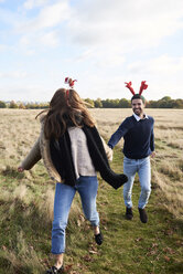 Glückliches, sorgloses Paar mit weihnachtlichem Kopfschmuck beim Laufen auf dem Lande - IGGF00829