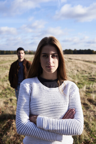 Junge Frau steht auf einem Feld mit einem Mann hinter ihr, lizenzfreies Stockfoto