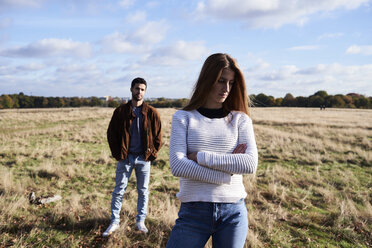 Ernste junge Frau steht auf einem Feld mit einem Mann hinter ihr - IGGF00837