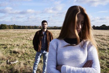 Ernste junge Frau steht auf einem Feld mit einem Mann hinter ihr - IGGF00838