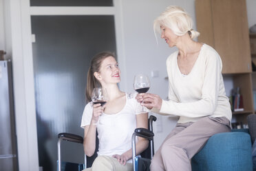 Mother and daughter in the wheelchair with a glass of red wine at home - SGF02339