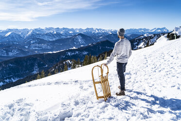 Deutschland, Bayern, Brauneck, Mann mit Schlitten im Winter in den Bergen mit Blick auf die Aussicht - DIGF05914