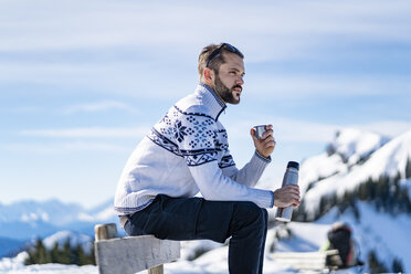 Germany, Bavaria, Brauneck, man sitting on bench in winter in the mountains having a break - DIGF05915