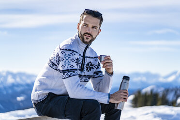 Germany, Bavaria, Brauneck, man sitting on bench in winter in the mountains having a break - DIGF05916