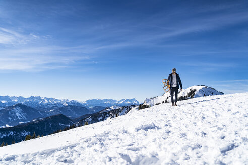 Deutschland, Bayern, Brauneck, Mann trägt Schlitten im Winter in den Bergen - DIGF05920