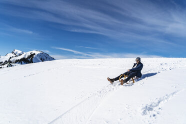 Deutschland, Bayern, Brauneck, Mann beim Schlittenfahren im Winter in den Bergen - DIGF05925