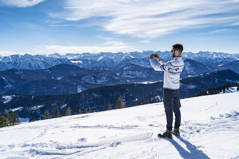 Deutschland, Bayern, Brauneck, Mann im Winter in den Bergen beim Fotografieren - DIGF05936