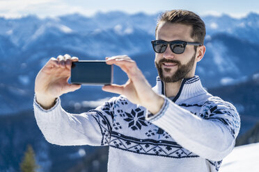 Deutschland, Bayern, Brauneck, Mann im Winter in den Bergen, der ein Selfie macht - DIGF05937