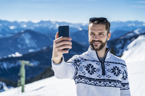 Deutschland, Bayern, Brauneck, Mann im Winter in den Bergen, der ein Selfie macht - DIGF05938