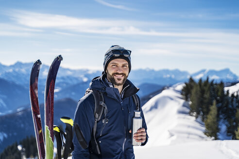 Germany, Bavaria, Brauneck, portrait of smiling man on a ski tour in winter in the mountains having a break - DIGF05961