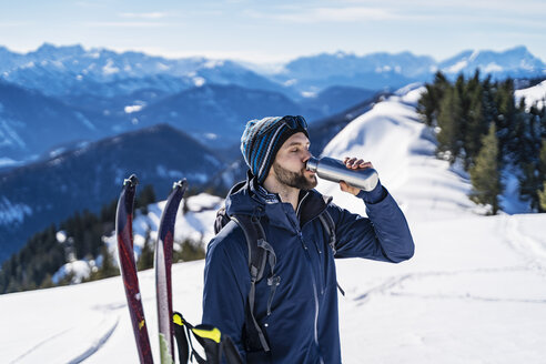 Deutschland, Bayern, Brauneck, Mann auf Skitour im Winter in den Bergen, der eine Pause macht und aus einer Thermoskanne trinkt - DIGF05962