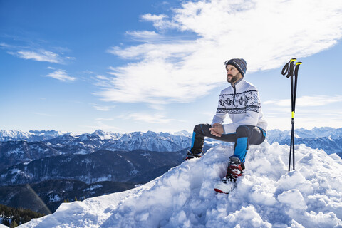 Deutschland, Bayern, Brauneck, Mann im Winter auf Berggipfel sitzend, lizenzfreies Stockfoto