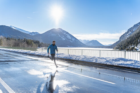 Deutschland, Bayern, sportlicher Mann läuft auf einer Straße im Winter - DIGF05973