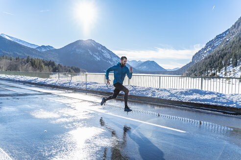 Deutschland, Bayern, sportlicher Mann läuft auf einer Straße im Winter - DIGF05974