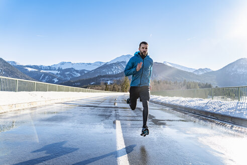 Deutschland, Bayern, sportlicher Mann läuft auf einer Straße im Winter - DIGF05975