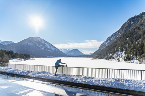 Deutschland, Bayern, sportlicher Mann streckt sich im Winter auf einem Brückengeländer, lizenzfreies Stockfoto