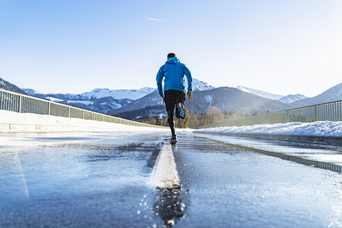 Deutschland, Bayern, sportlicher Mann läuft auf einer Straße im Winter - DIGF05982