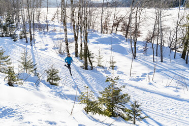 Germany, Bavaria, sportive man running through snow in winter - DIGF05994