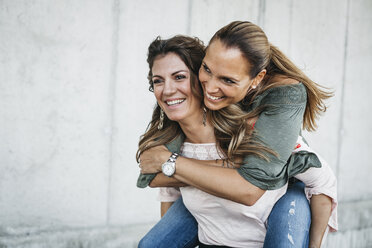 Portrait of laughing woman giving her friend a piggyback ride - HMEF00245