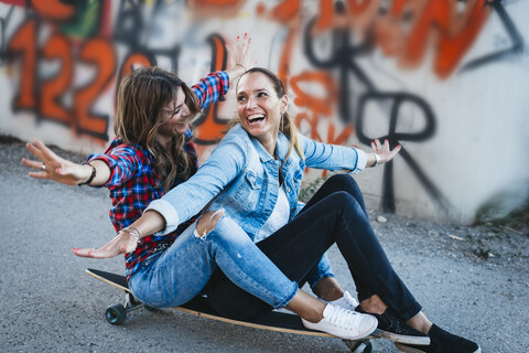 Zwei lachende Freunde sitzen mit ausgestreckten Armen auf einem Longboard, lizenzfreies Stockfoto