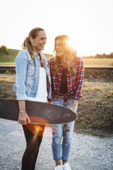 Zwei lachende Freunde mit Longboard bei Sonnenuntergang - HMEF00256