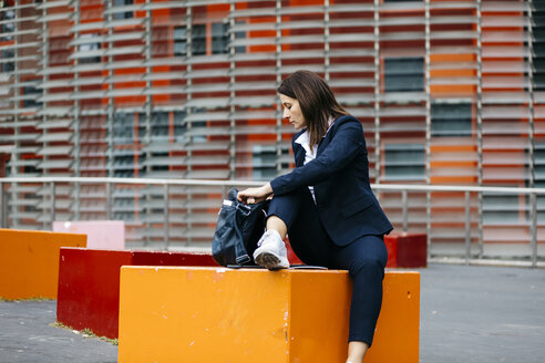 Geschäftsfrau sitzt vor einem Bürogebäude in der Stadt und sucht nach etwas in der Tasche - JRFF02727