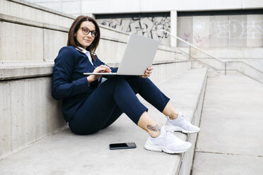 Porträt einer Geschäftsfrau, die im Freien auf einer Treppe sitzt und einen Laptop benutzt - JRFF02742