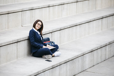 Porträt einer lächelnden Geschäftsfrau, die mit einem Laptop auf einer Treppe im Freien sitzt - JRFF02746