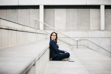 Businesswoman sitting outdoors on stairs with laptop - JRFF02747