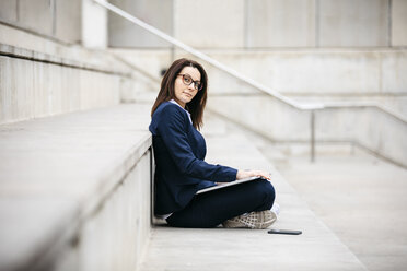 Porträt einer Geschäftsfrau, die mit einem Laptop auf einer Treppe im Freien sitzt - JRFF02748