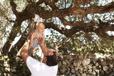 Father playing with little boy outdoors under a tree - IGGF00869