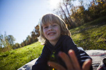 Porträt eines lächelnden kleinen Jungen auf einer Decke im Freien - JLOF00311
