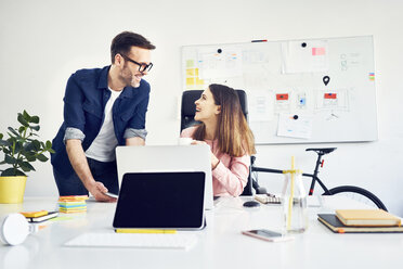 Two colleagues working together on laptop in office - BSZF00992