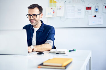 Lässiger Geschäftsmann bei der Arbeit am Laptop am Schreibtisch im Büro - BSZF01013