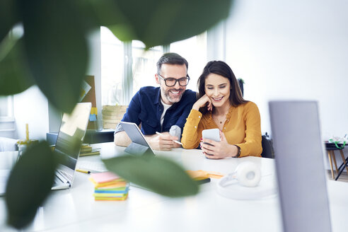 Zwei Kollegen arbeiten mit Tablet und Smartphone im Büro zusammen - BSZF01032