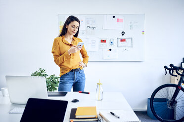 Geschäftsfrau hält Smartphone an Whiteboard im Büro - BSZF01039