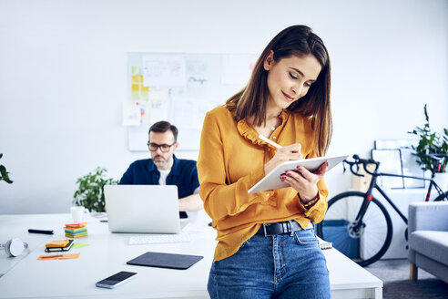 Businesswoman using tablet in office with colleague in background - BSZF01040