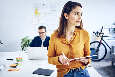 Geschäftsfrau hält Tablet im Büro mit Kollegen im Hintergrund, lizenzfreies Stockfoto